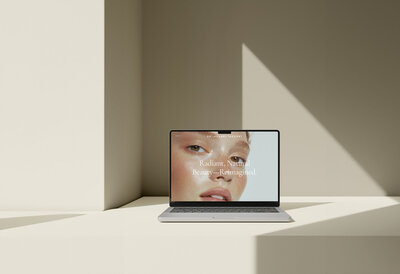 Laptop on a sunlit table displaying a beauty image and branded tagline, reflecting a strategic aesthetic medicine brand identity and website design.