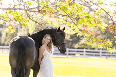 a photo of a girl leaning against a black horse with flowery orange trees hanging behind them