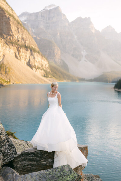 Bride standing on a rock at Peyto Lake in Banff National Park with turquoise water and golden mountains in the background at sunset captured as a warm and scenic summer bridal portrait
