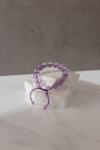 A stunning deep purple amethyst crystal bead bracelet on a quartz sphere.