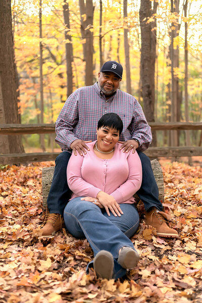 Husband sitting on wooden log and wife sitting on ground in a park