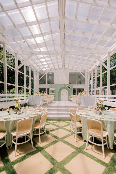 Airy white pavilion set with round sage linens, pastel florals, and white cane-back chairs on a patterned lawn in Houston.