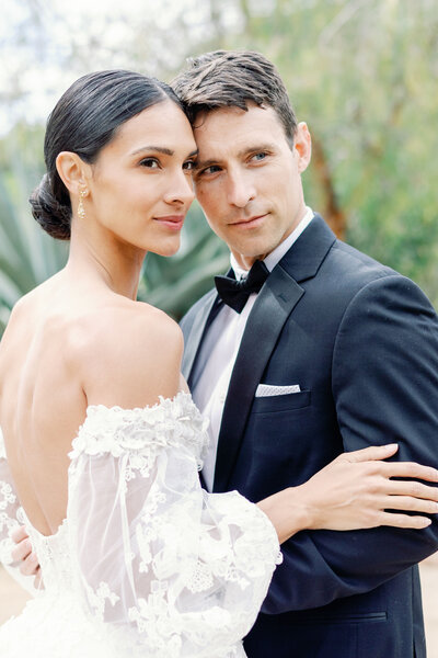 bride with a slicked back bun in a low back wedding dress holds her groom at their outdoor California wedding venue captured by bay area photographers