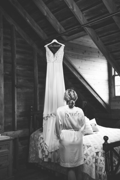 Bride glances up at her  wedding dress that's hanging from the ceiling.