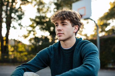 captivatingly handsome young man poses for senior pictures Pittsburgh pa against a setting sun and a basketball hoop.