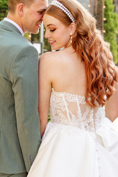 Redheaded bride shows off her beautiful lace dress while snuggling with groom