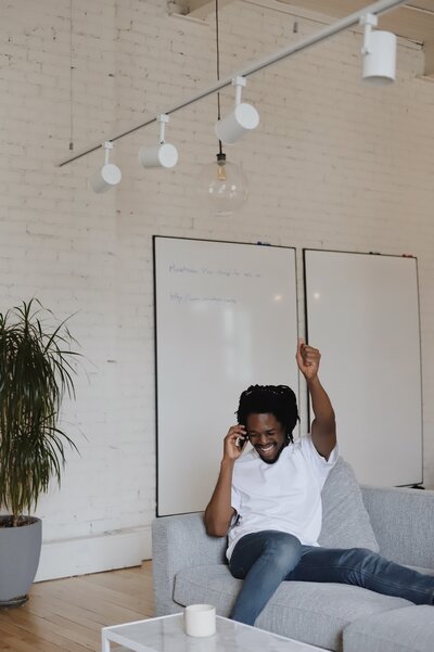a black man celebrating as he is on the phone sitting on couch