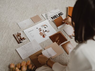 Design moodboard with various print materials in neutral tones, featuring abstract shapes, textures, and typefaces spread across a cozy rug.