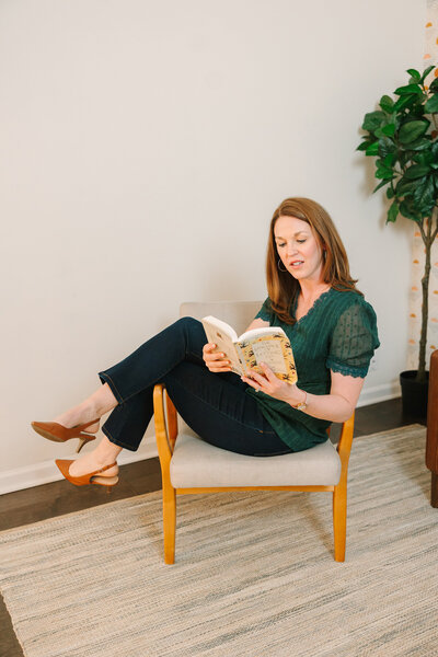 Lindsay playfully sitting on a chair, reading a book