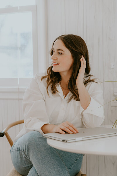 Rachel Haselwander, OBM and owner of Agera Business Services leaning against a couch and smiling