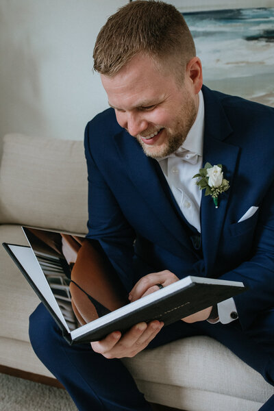 Groom smiling at little black book from bride by Boudoir by Kiella
