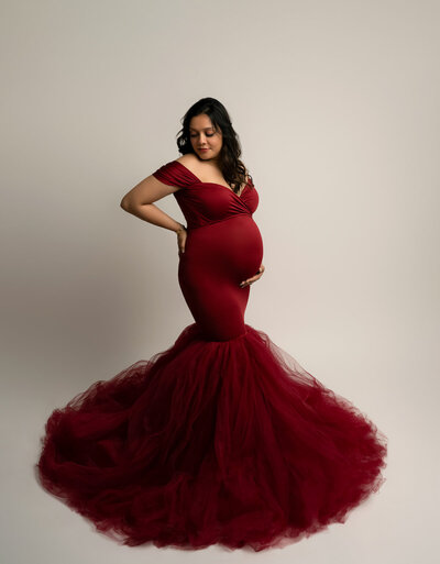 Form-fitting red dress with ruched detail and dramatic train in studio lighting – Austin maternity session
