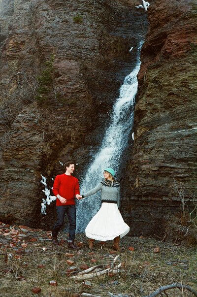 bride in wool sweater leads groom past a waterfall during Newfoundland elopement