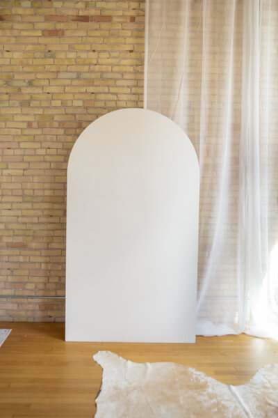Seven foot white wooden arch backdrop against a brick wall.