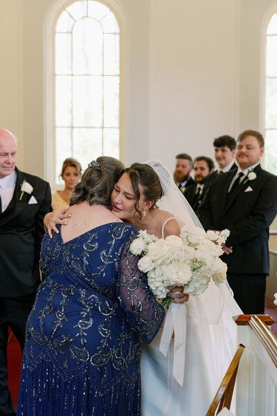 Bride hugging her mother during a heartfelt ceremony moment inside a Michigan church, captured with candid and emotional wedding photography.