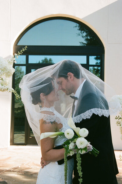 Bride and groom kiss under the bride’s lace veil outside Rosebridge Estate, an Austin wedding venue, editorial fine art film-inspired portrait by a Texas and destination wedding photographer.

