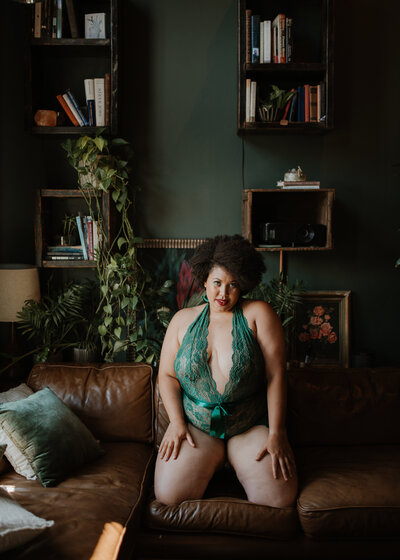 Woman in green lingerie poses on a couch in front of an art wall in the Vancouver, BC boudoir studio.