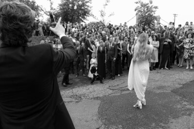 black and white image by photographer tom thornton of bride facing crowd on wedding day groom in foreground