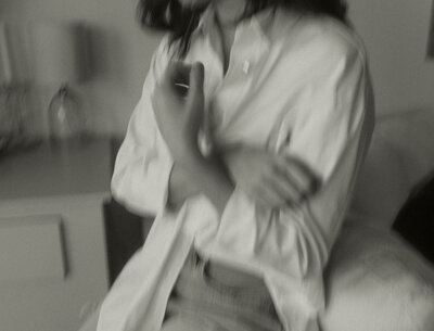 Blurry black and white photo of womans arms crossing in front of her button down shirt while she leans back on a couch