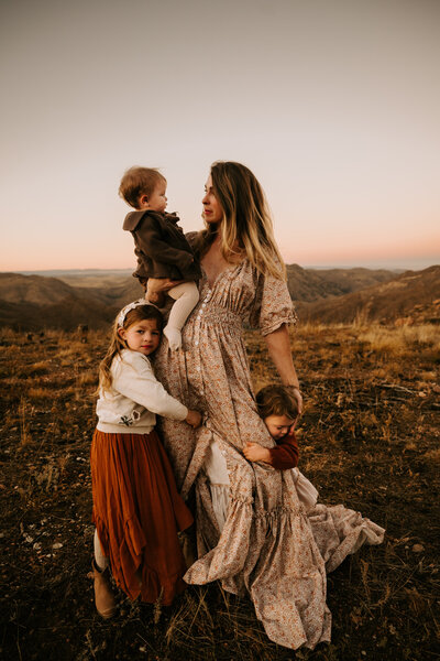 A mom in a flowing dress cuddling with her three daughters in Rist Canyon by Grey Rock