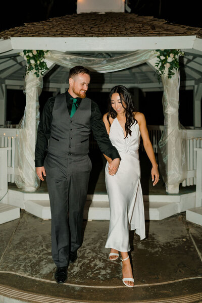 wedding couple holding hands and walking out of a gazebo at night
