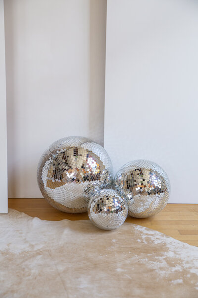 Three different size disco balls sitting on the floor.