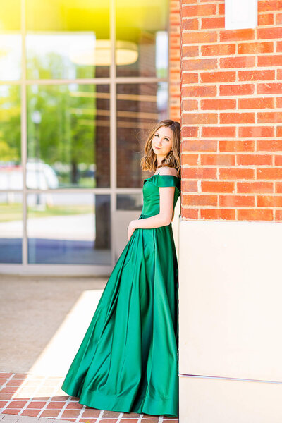 A girl in a green prom dress poses in front of some windows