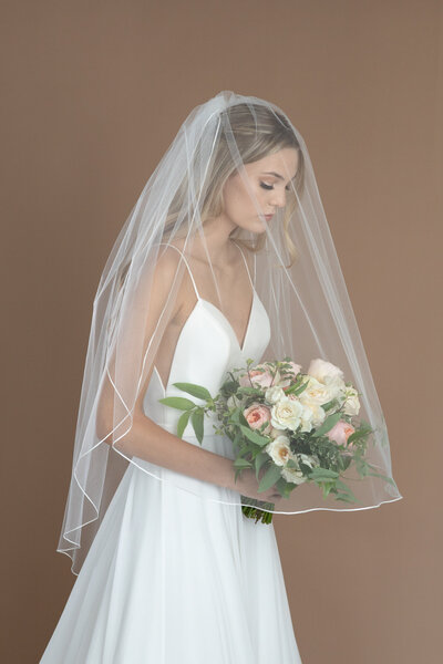 Bride wearing a two layer fingertip length veil with ribbon edge, and holding a white and blush bouquet