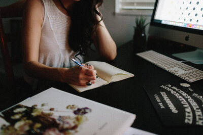 Miranda writing in a notebook at a desk with a plant in the background.