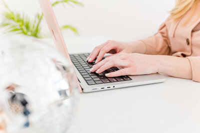 lady sitting at desk typing on computer with disco ball in the corner as well as plant