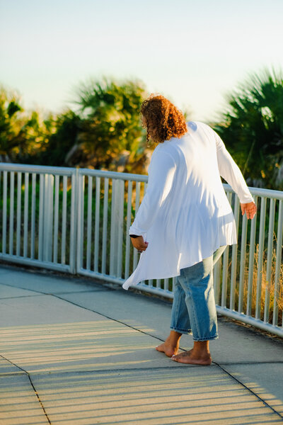 Certified life coach Claudine Martinell walks barefoot in white; get in touch to embark on your transformational journey.