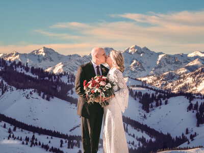 Stunning photograph capturing a bride and groom sharing a tender kiss amidst the majestic mountains, epitomizing the grandeur and romance of their special day.