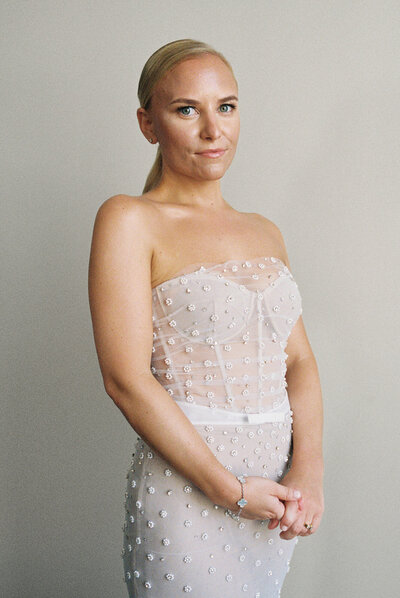 Blonde bride softly smiles at camera while showing off details of her elegant beaded gown