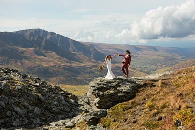 Bride and Groom dance with bouquet in hand on a rock overlooking  Hatcher Pass, Alaska.