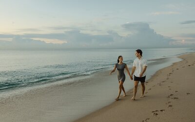 couple holds hands and walks along beach in south florida