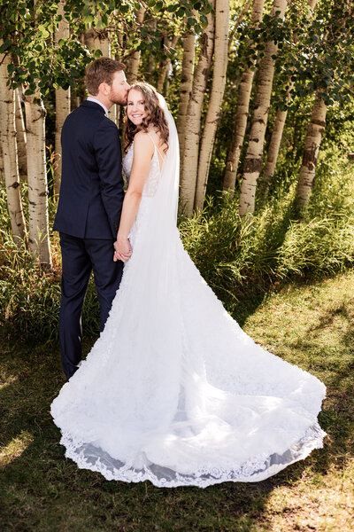 groom kisses brides temple as she looks back and smiles at the camera