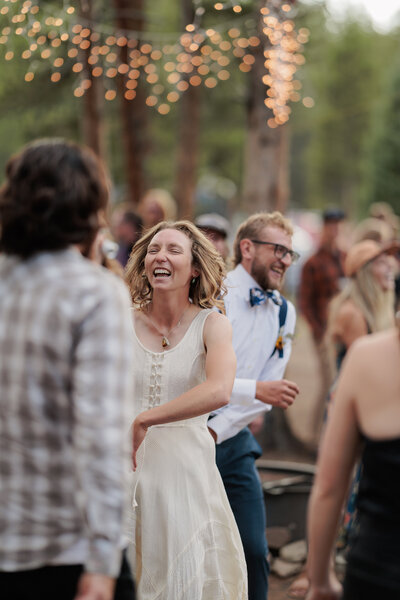 A bride and groom dancing with their friends in the forest, fairy lights strung above them