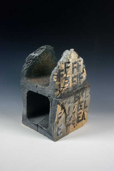 A cinder block that was hand made out of clay is decorated with underglaze to resemble graffiti and various other imagery