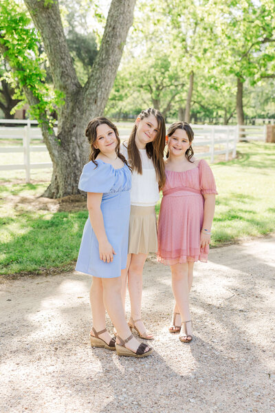 Three sisters wearing colorful dresses near trees in Fulshear Texas