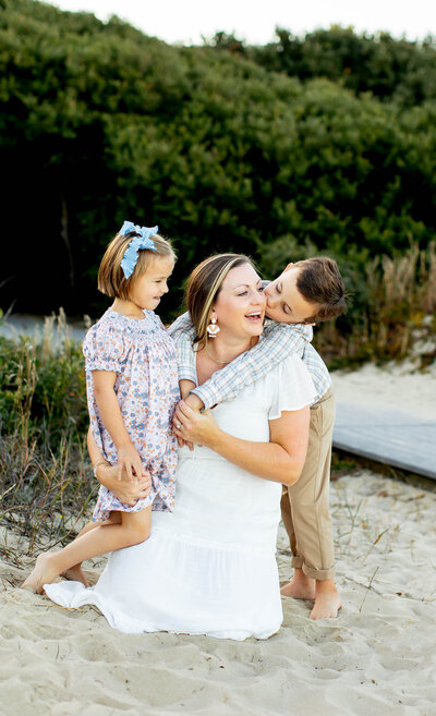 Tender moment captured by Brooke Tucker of a mother and her two children sharing a quiet embrace during a beachside session in Coastal Virginia