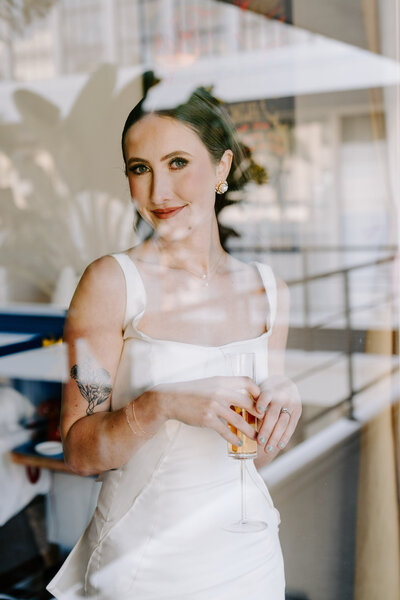 bride holding champagne glass behind glass