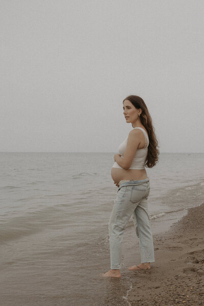 A photo of a pregnant woman on the beach. she is embracing her growing belly as she stares out over lake erie in western new york. Photo by Dash and Boheme Photography. 