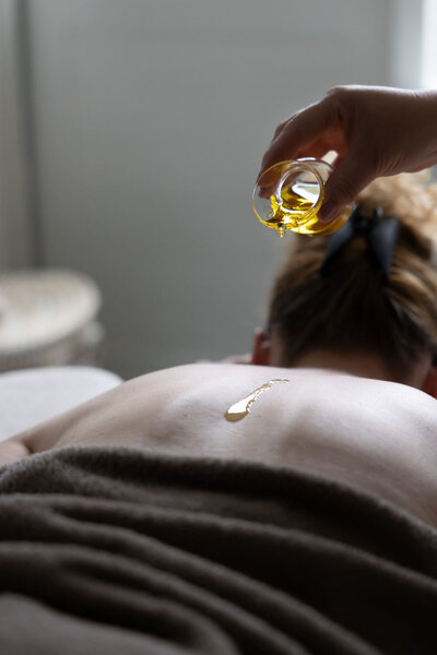 Massage olie wordt gedruppelt op rug van een client. Natuurlijke olie. In beeld brengen van werkwijze. Storytelling © Studio Ensō