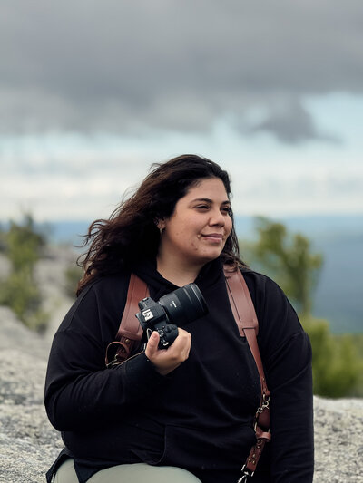 a photographer holding a professional camera looking out over a mountain top 