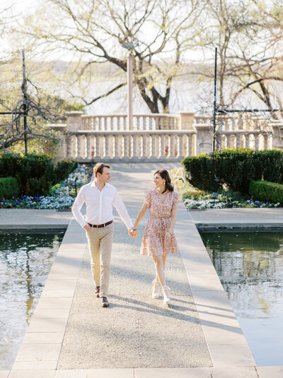 couple walk together in short pink spring dress and white shirt and khaki pants at Dallas Arboretum in Dallas, Texas