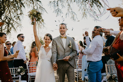 A newlywed couple walks as friends throw olive leaves after the civil ceremony, Fattoria Lavacchio.