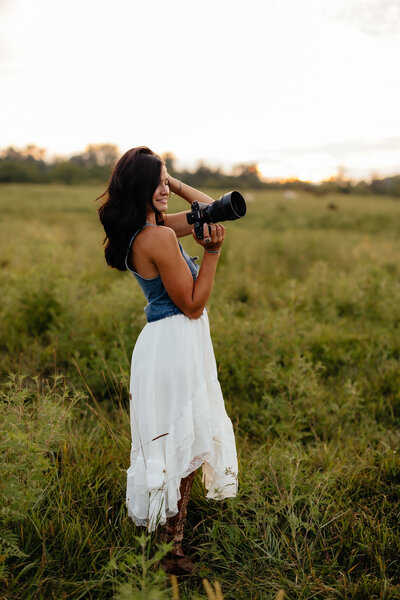 woman holding camera while smiling in a field 