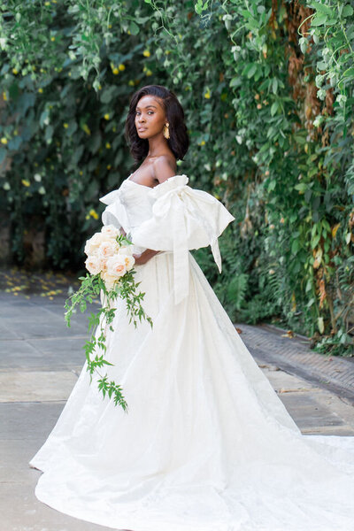 A beautiful black bride wearing a custom dress with puff sleeves holding a boutquet by All For Love London at Sezincote House in the Cotswolds