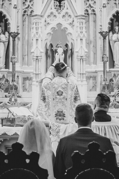 Bride and groom kneel before the altar as the host is elevated and consecrated at their wedding Mass.