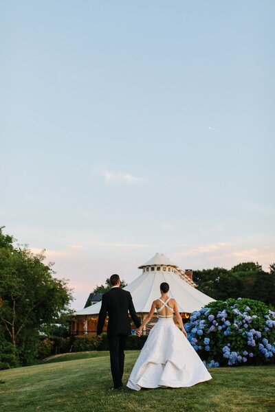 a bride and groom walk into there wedding reception in a tent